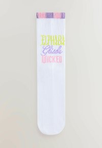 Vit ankelsocka med färgglad ribbad topp. Har orden "ELPHABA", "Glinda" och "WICKED" i olika pastellfärger och typsnitt.
