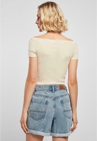 Beige off-shoulder top och ljusblå denimshorts med uppvikta fållar; har bakfickor och en brun läderetikett vid midjan.