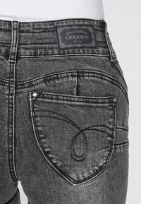 Jeans de mezclilla negros con un bolsillo trasero en forma de corazón, una etiqueta de cuero con marca en la cintura y detalles de costura en contraste.