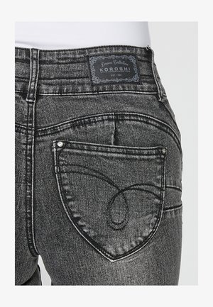 Fekete farmernadrág szív alakú hátsó zsebbel, márkás bőr címkével a derekán és kontrasztos varrási részletekkel.