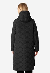 Abrigo acolchado negro con capucha, con una textura ondulada y un diseño largo. La vista trasera destaca la costura con patrón.
