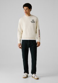 Creme sweatshirt met "RED BULL RACING" grafische opdruk, zwarte tekst op de borst en mouw. Draag het met donkere jeans en witte sneakers.