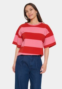 Kortærmet T-shirt med røde og lyserøde vandrette striber, rund hals, afslappet pasform, lavet af bomulds materiale, parret med mørkeblå højtaljede bukser.