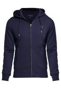 Sweat à capuche zippé marine en tissu mélangé coton. Comprend une grande capuche, des poches avant, des poignets côtelés et un logo discret sur la poitrine.