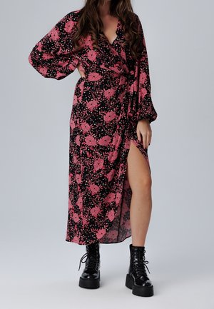 Zwarte jurk met een roze bloemenpatroon, V-halslijn en lange mouwen. De jurk heeft een zijsplit en is gecombineerd met chunky zwarte veterlaarzen.