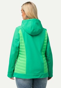 Vihreä takki, jossa on huppu, sileä kangas ja kevyet, vihreät vuorikankaat sivuilla. Suunniteltu rentoon käyttöön, jossa on väljä istuvuus.