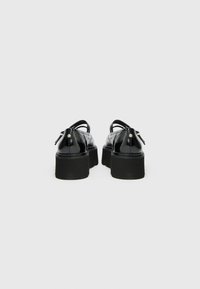Black patent leather shoes with a thick black sole, featuring a rounded design and a back zipper closure. Smooth, glossy finish.