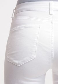 Vita denimjeans med medelhög midja och klassisk femfickorsdesign, där bakfickan har ett chevronstygnmönster.