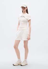 Ροζ στενή μπλούζα με τύπωμα "TOMMY JEANS", σε συνδυασμό με λευκά σορτς. Φορεμένη με αντίστοιχο καπέλο και μπεζ αθλητικά παπούτσια.