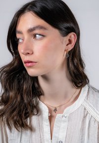 Guldörhängen med en liten ormdesign, tillsammans med ett fint guldhalsband med en liknande berlock, buren av en modell.