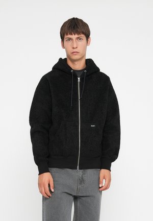 Black hooded jacket with a fuzzy texture, front zipper, and kangaroo pockets. Features a logo on the left pocket and ribbed cuffs.