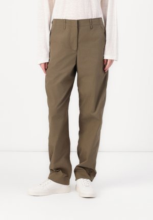 Pantaloni beige a gamba dritta in twill di cotone, con zip, passanti per la cintura e tasche laterali, abbinati a scarpe da ginnastica bianche.