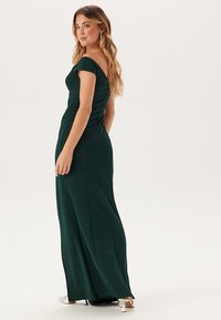 Robe de soirée longue, vert foncé, avec des manches dénudées, un corsage ajusté et une jupe fluide, présentant un tissu lisse et de subtils détails de couture.