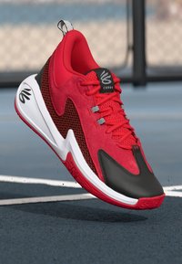 Red athletic shoe with suede and mesh materials, featuring a black rubber sole, white midsole, and a logo on the tongue.