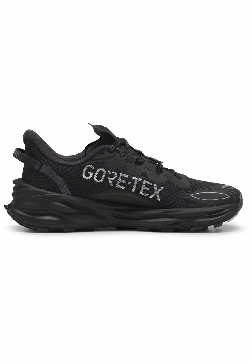 Baskets de course noires avec une tige en maille texturée, mettant en avant un logo "GORE-TEX" bien visible. La semelle est épaisse avec un design en vagues et des motifs de traction.