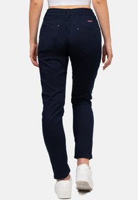 Pantalons moulants bleu marine avec une taille élastique, dotés de deux poches arrière avec des coutures décoratives et portés avec des baskets blanches.