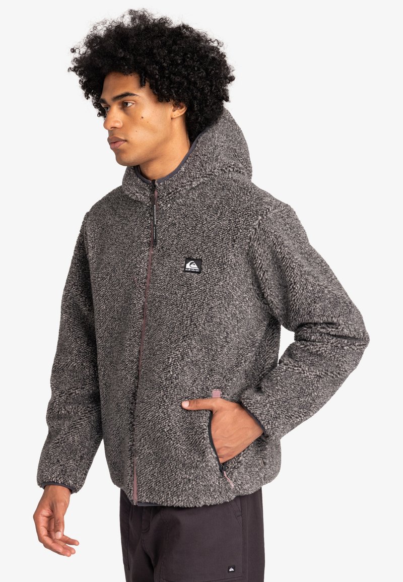 Veste en polaire gris foncé avec une finition texturée, fermeture éclair intégrale, poches avant et capuche attachée. Comprend un patch logo sur la poitrine.