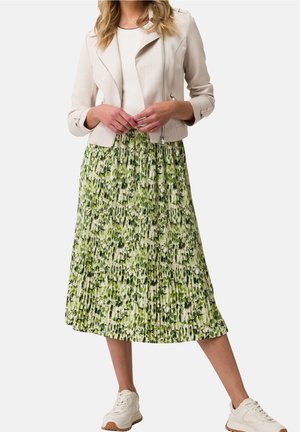 Veste en cuir synthétique crème avec détails zippés, associée à une jupe plissée à motifs floraux verts et à des baskets blanches. Motifs texturés dans différentes nuances de vert.