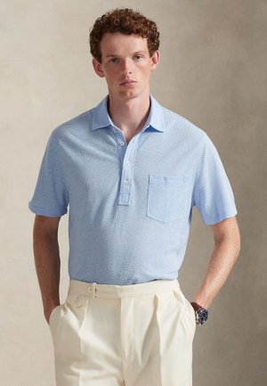 Polo azzurro chiaro con finitura testurizzata, maniche corte, colletto e tasca frontale, abbinata a pantaloni color crema.