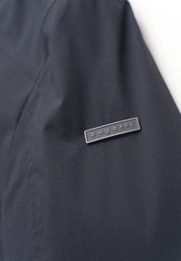 Navy Blaumann mit glatter Textur, ausgestattet mit einem silberfarbenen Metallschild, auf dem "bugatti" auf dem linken Ärmel eingraviert ist.