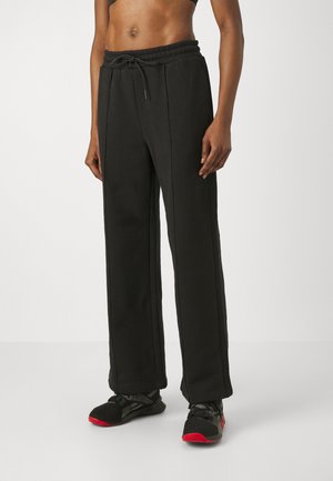 Pantalons de jogging larges noirs avec une taille à cordon de serrage, en coton, présentant des coutures verticales et une texture lisse.