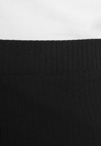 Tissu côtelé noir avec une large ceinture élastique, comportant une section blanche lisse au-dessus, mettant en valeur des textures et des couleurs contrastées.