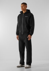 Hoodie zippé noir avec poches avant et logo. Associé à un pantalon fuselé assorti avec taille à cordon de serrage et accents blancs.