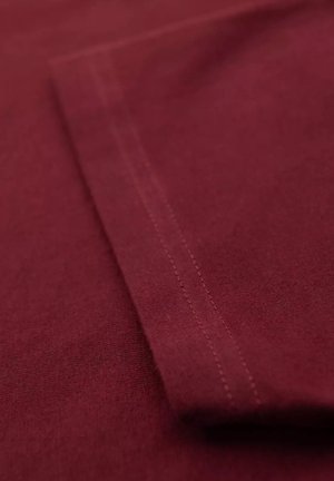 Tissu bordeaux à texture lisse, présentant des coutures visibles le long du bord et un pliage plat.