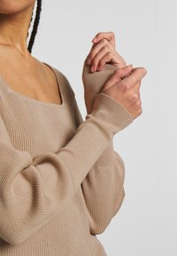 Beige ribbed Langarmtop mit quadratischem Ausschnitt. Verfügt über figurbetonte Ärmel mit Daumenlöchern und einem weichen, strukturierten Stoff.