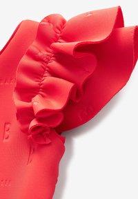 Tessuto rosso con accentuazioni arricciate, caratterizzato da un design testurizzato. Il materiale appare liscio e leggermente elasticizzato, con lettere in rilievo.