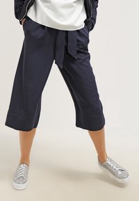 Námořnické cropped kalhoty s vázačkou v pase, texturovaná tkanina a široký střih, spárované se stříbrnými teniskami s texturovaným svrškem a bílými podešvemi.