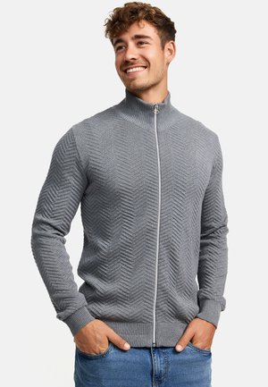 Gray zip-up sweater with a textured herringbone pattern, ribbed cuffs and hem, paired with blue jeans, worn with hands in pockets.