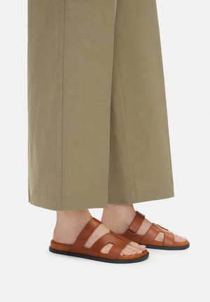 Sandalias de cuero marrón con múltiples tiras y diseño de punta abierta, combinadas con pantalones anchos khaki crop en una tela lisa.