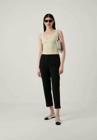 Top de alças amarelo claro com relevo, calças pretas ajustadas e sapatos planos com um design preto e prateado. Os acessórios incluem óculos de sol e uma bolsa prateada.