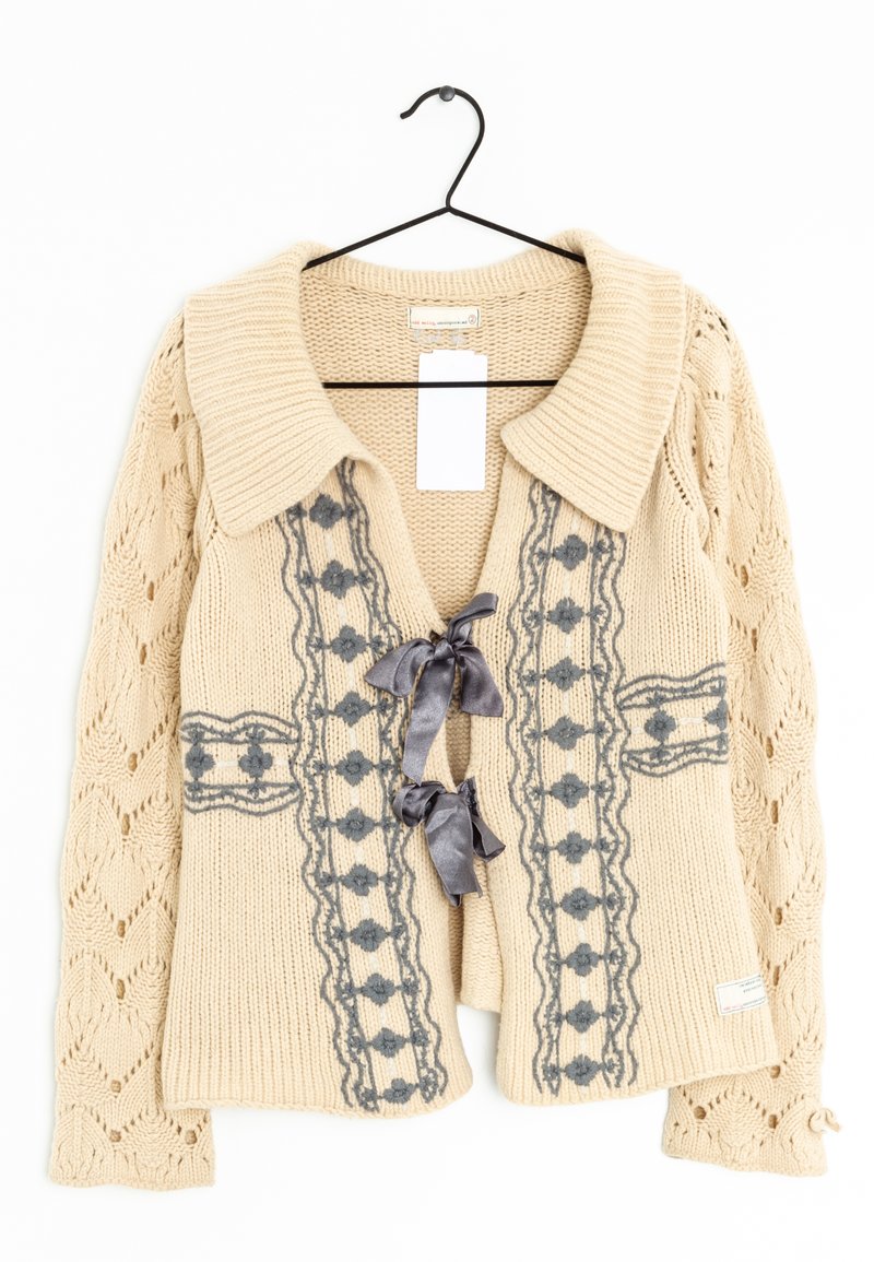 Cárdigan beige de punto con un cuello ancho, bordado floral gris y lazos de cinta. Presenta una textura estampada y mangas con un trabajo de encaje intrincado.