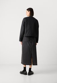 Černá bomber bunda s kratším střihem, zkombinovaná s dlouhou tmavě modrou denimovou sukní s rozparkem na zadní straně. Černé boty dokončují outfit.