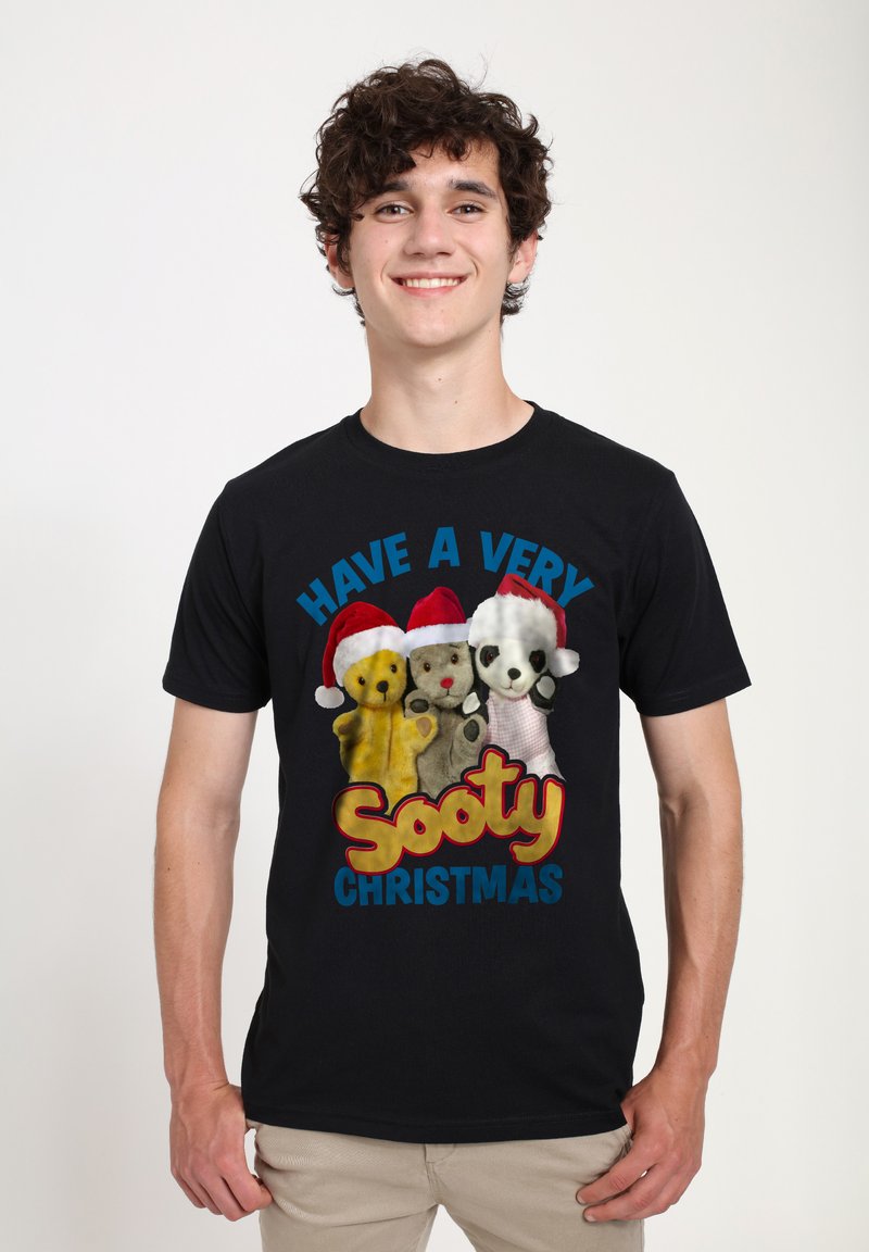 Sort T-shirt med tre dukkefigurer iført røde nissehuer. Teksten lyder "HAV EN MEGET Sooty JUL" i farverige bogstaver.