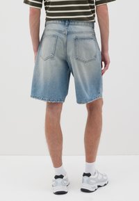 Shorts de mezclilla azul claro con un corte relajado, que cuentan con bolsillos traseros y dobladillos desgastados, combinados con zapatillas grises y calcetines blancos.