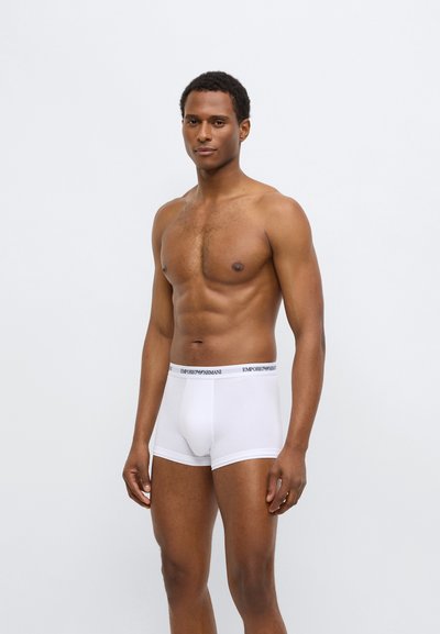 Boxers blancs en coton avec une coupe ajustée et une ceinture élastique portant le logo "Emporio Armani". Texture lisse, style minimaliste.