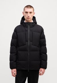 Jachetă puffer neagră cu glugă, având un fermoar frontal, design matlasat și panouri mari orizontale. Materialul pare neted și izolat.