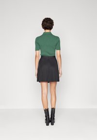 Maglietta polo lavorata a maglia verde abbinata a una gonna plissettata nera, completata da stivali neri con tacco al ginocchio. Tessuti lisci, design semplice.