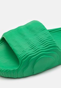 Grønn gummislidesandal med en teksturert, bølgete overdel og en rillet såle, designet for komfort og enkel bruk.