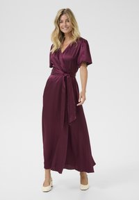 Puvu wrap-kjole laget av glatt stoff, har korte pufferm, en tettsittende midje med belte, og en flytende, ankel-lengde skjørt.
