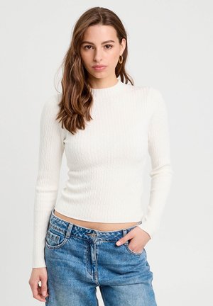 Witte geribbelde gebreide trui met lange mouwen en een ronde hals, gecombineerd met blauwe high-waisted jeans. Soepele textuur en aangesloten ontwerp.