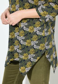 Blusa a fiori in blu navy con pois gialli, verdi e bianchi; presenta un orlo asimmetrico e maniche a tre quarti.