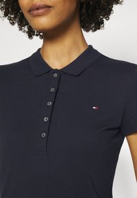 Navy blue polo paita, joka on valmistettu teksturoidusta kankaasta. Siinä on klassinen kaulus, lyhyet hihat ja pieni punavalkoinen brodeerattu logo.