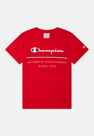 Camiseta de algodón roja con el logo "Champion" en blanco y negro, con el texto "AUTÉNTICA ROPA DEPORTIVA DESDE 1919" impreso debajo.