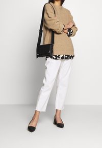 Beige stickad tröja, svart och vit mönstrad skjorta under, vita cropped jeans, svart handväska och svarta spetsiga klackar.