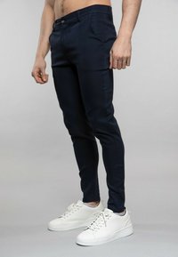 Pantalons ajustés navy avec une texture lisse et des poches avant, associés à des baskets blanches à bout rond et à semelle plate.