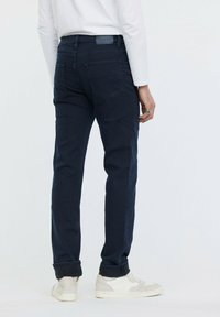 Jeans de mezclilla oscuro en color navy con corte slim, cinco bolsillos, un dobladillo ligeramente enrollado y una etiqueta de cuero en la cinturilla.